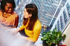 A conversation between two women of different nationalities during a meeting at work in a high office building.