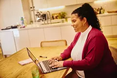 Female, smiling, working on laptop in kitchen on a kitchen table