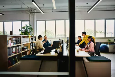 People working at an office setting, sitting behind a computer